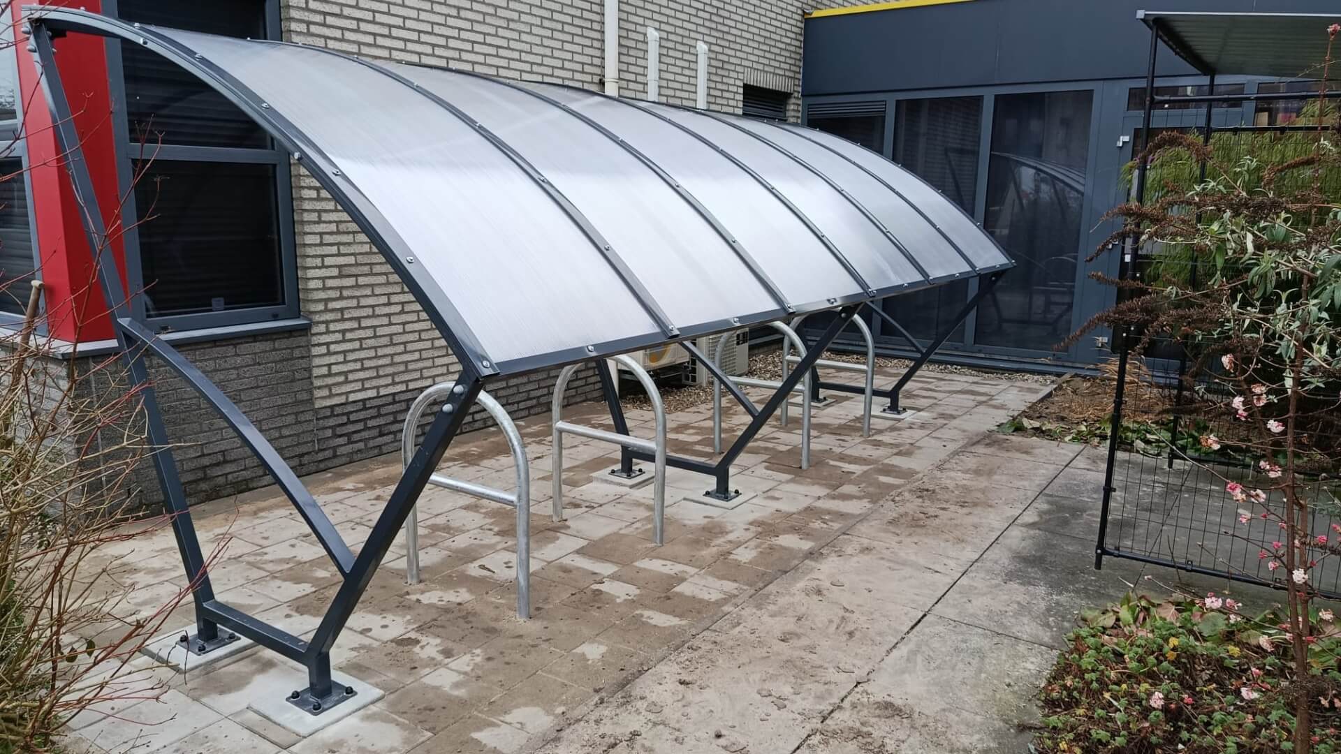 Bouwpakket Fietsoverkapping van 5 meter in RAL 7016 antraciet geleverd in Woerden – stalen fietsparkeeroverkapping met gebogen dakconstructie naast bedrijfspand
