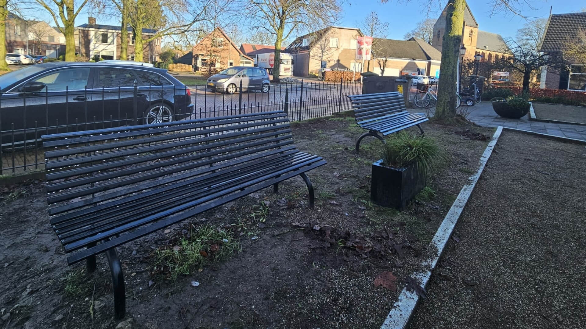 2 parkbanken geplaatst op een grasveld met op de achtergrond een kerk en auto's