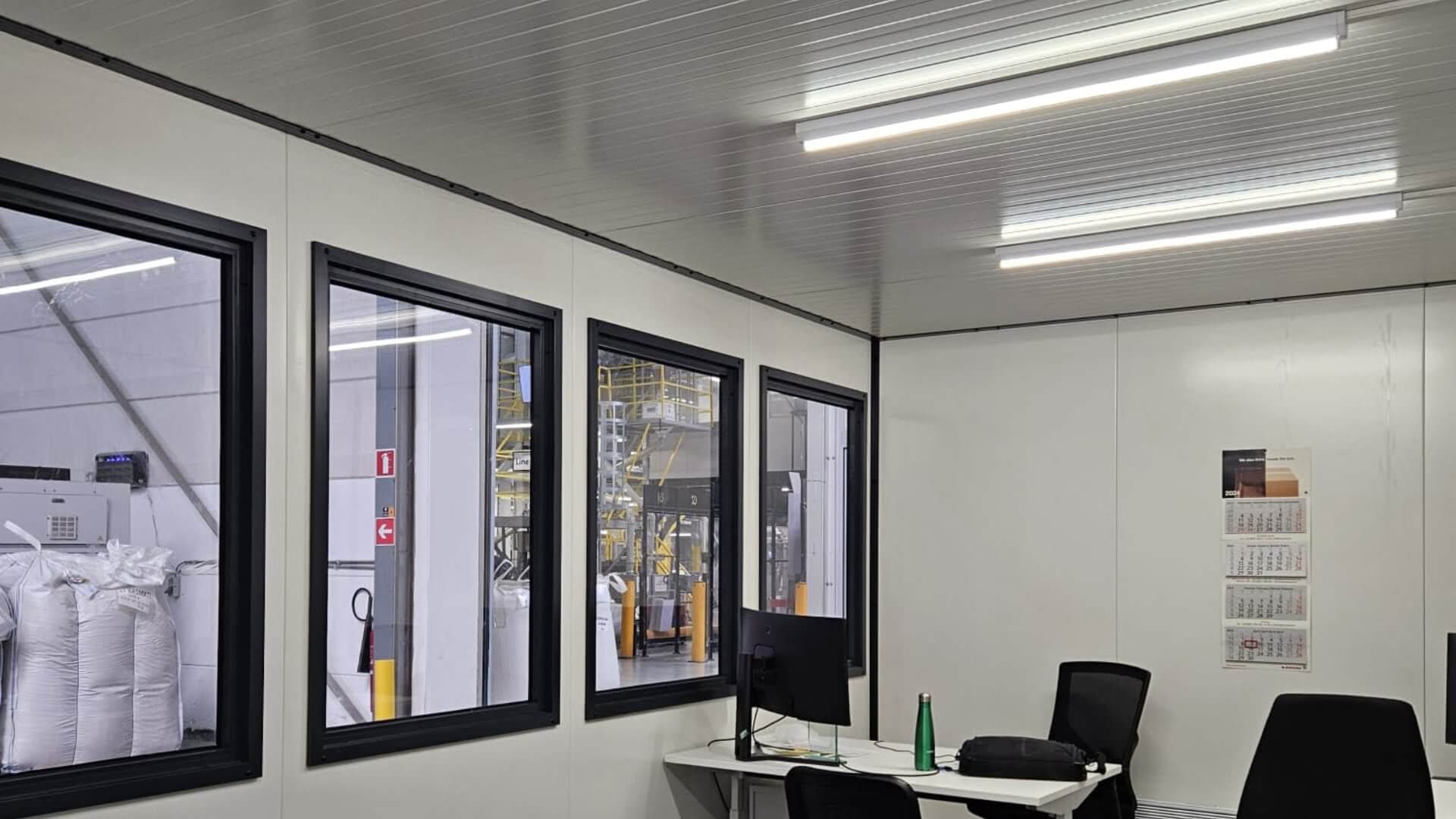 Interieur van een modulaire kantoorunit met ramen, bureaus en TL-verlichting in een magazijn