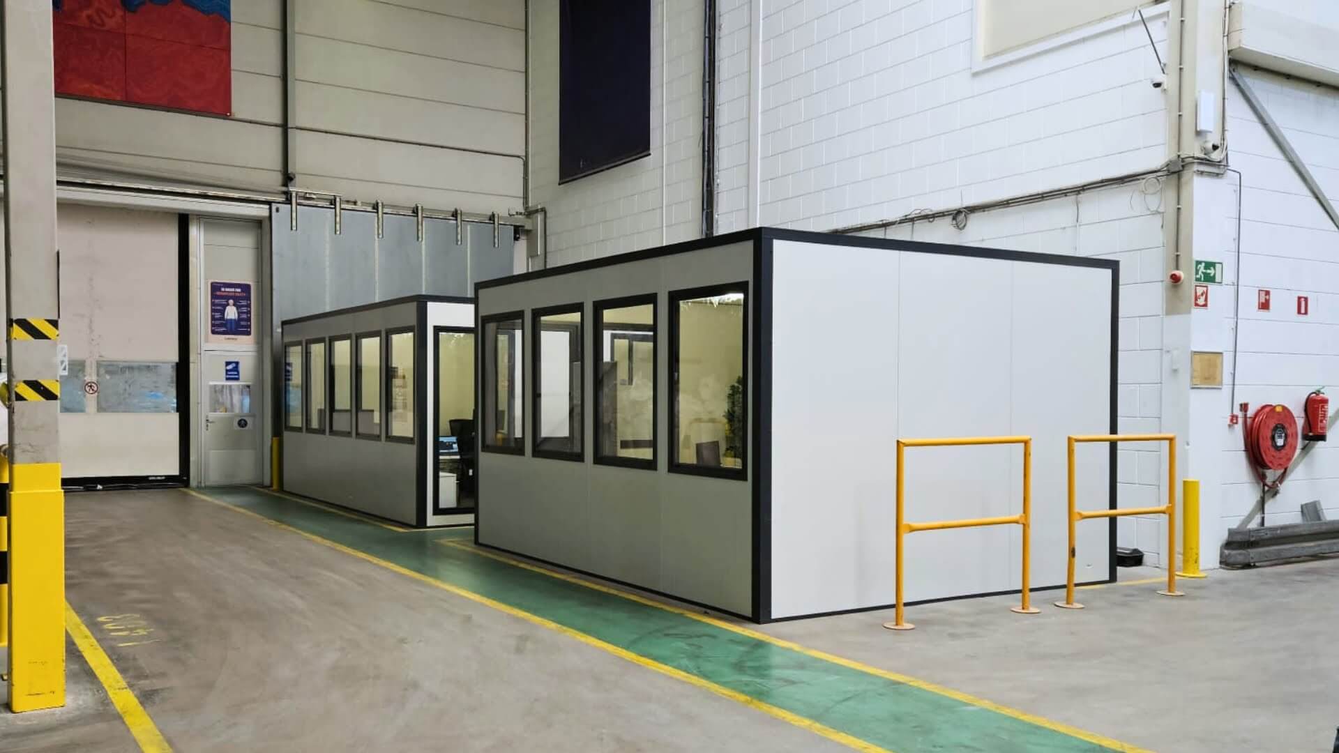 Modulaire kantoorunit in magazijnomgeving met ramen en afgesloten werkruimte.
