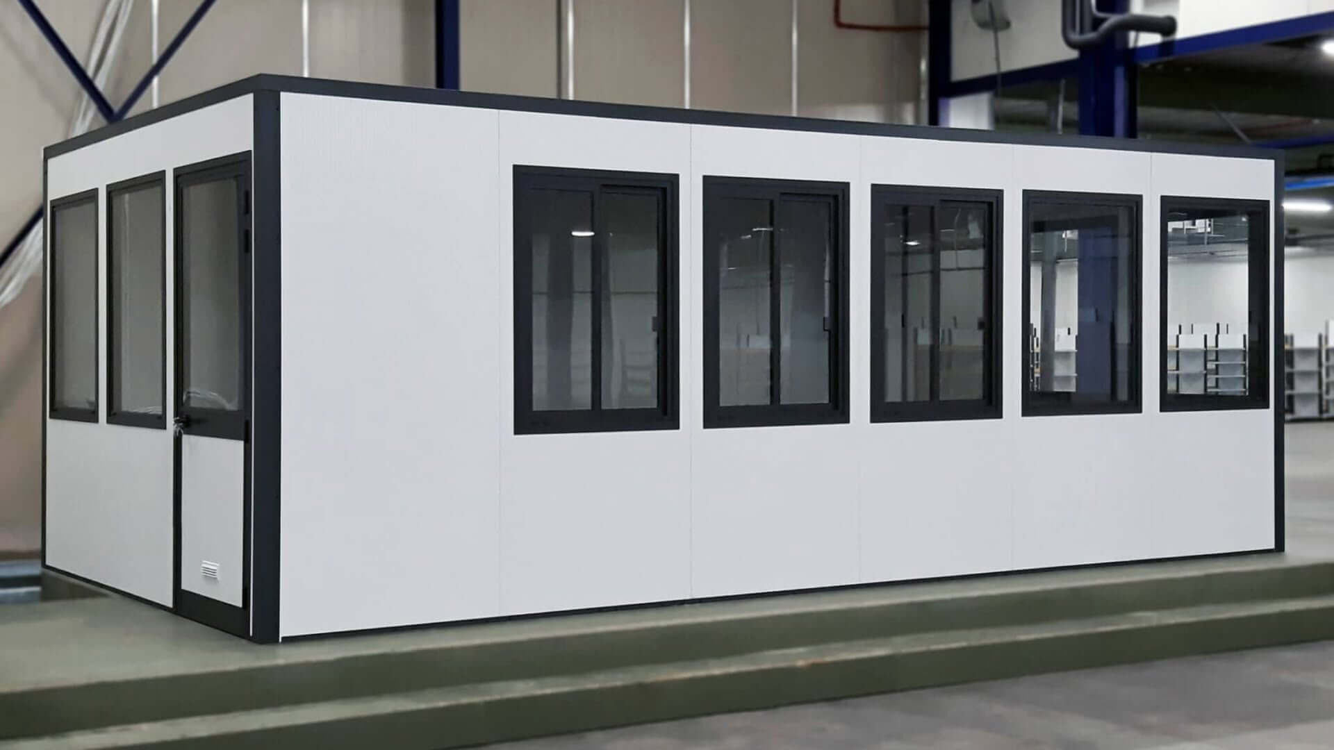 Zelfbouw kantoorunit met ramen en deur, geplaatst op een verhoging in een bedrijfshal.