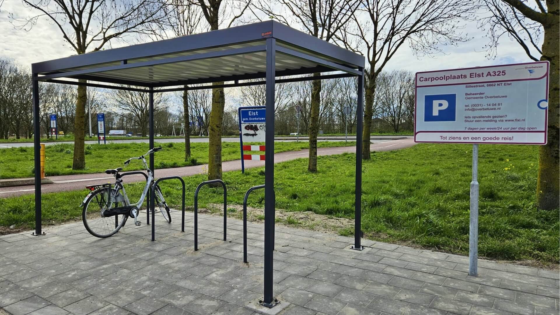 Fietsoverkapping met staanders in ral-kleur en fietsnietjes op carpoolplaats Elst A325 met informatiebord.