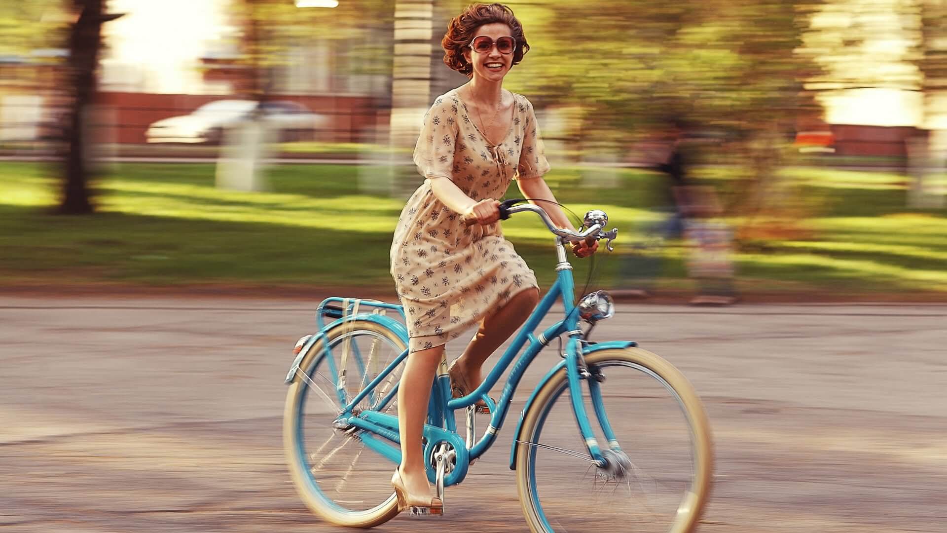 Vrolijke vrouw met jurk aan op een blauwe fiets umfeldt