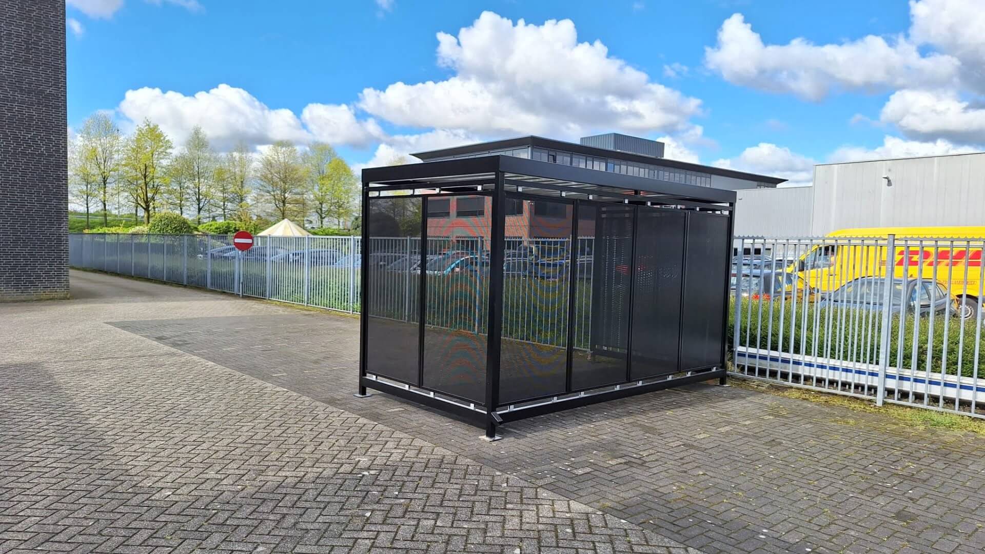 Fietsoverkapping voor bedrijven met een maatvoering van 4x2 meter, in kleur antraciet en verankerd op tegels bij een bedrijventerrein.