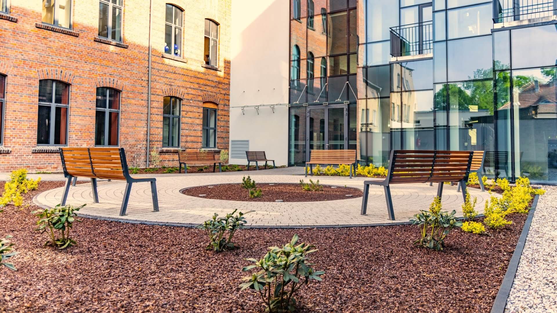 Meerdere houten parkbanken met stalen onderstel in een moderne binnentuin van een gebouw met glazen gevel.
