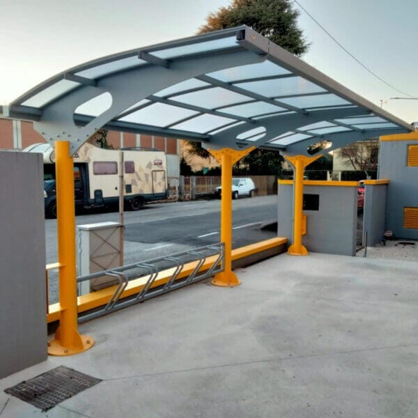 Overdekte rijwieloverkapping Larus kopen Overdekte fietsenstalling met gele stalen palen, grijs dak en geïntegreerd fietsenrek op een betonnen ondergrond.