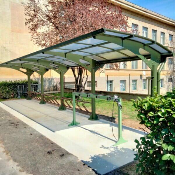 Rijwieloverkapping in RAL-kleur bestellen voor stallen van fietsen Rijwieloverkapping met stallen frame in groen en voorzien van polycarbonaat dak, geplaatst naast kantoor op beton.