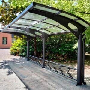 Moderne stalen fietsenoverkapping met gebogen dak en geïntegreerd fietsenrek.