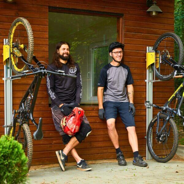 Fietsenrek muurbevestiging voor mountainbikes Mountainbikes in verticale wandhouders met lift, gemonteerd op houten gevel, bikers in gesprek