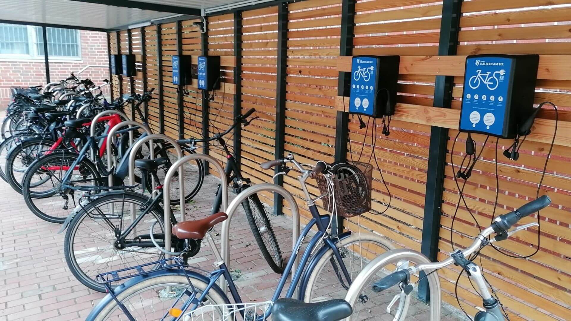 Overdekte fietsenstalling met meerdere e-bikes en oplaadpunten aan een houten wand