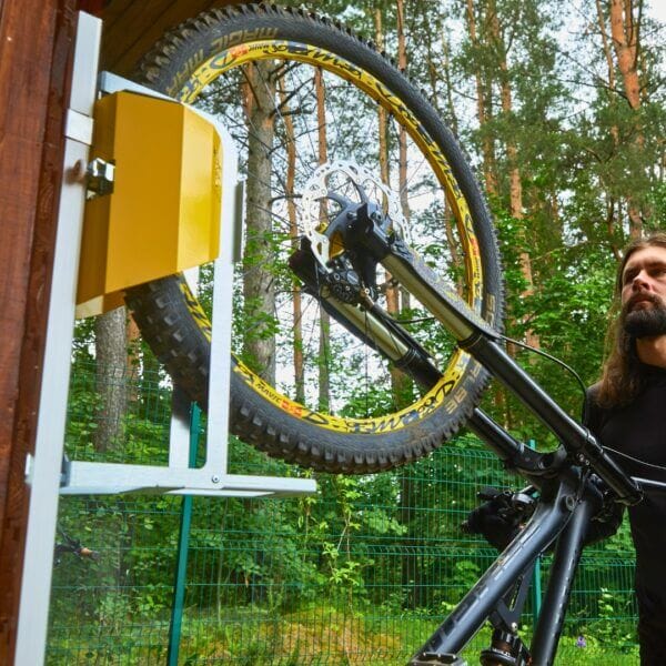 hangend-fietsrek-mountainbike-opslag Close-up van verticale fietsenrek met gele lift, wandmontage op houten wand en mountainbike in houder