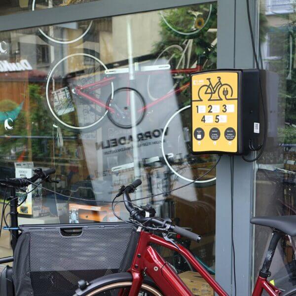 Laadstation voor elektrische fietsen, wandgemonteerd bij een fietsenstalling, met meerdere oplaadpunten.