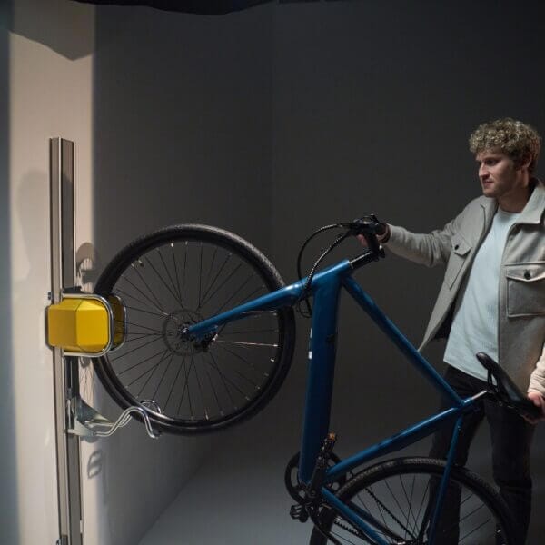 man-gebruikt-fietsophangsysteem Man plaatst fiets in fietsenrek muur met gele lift