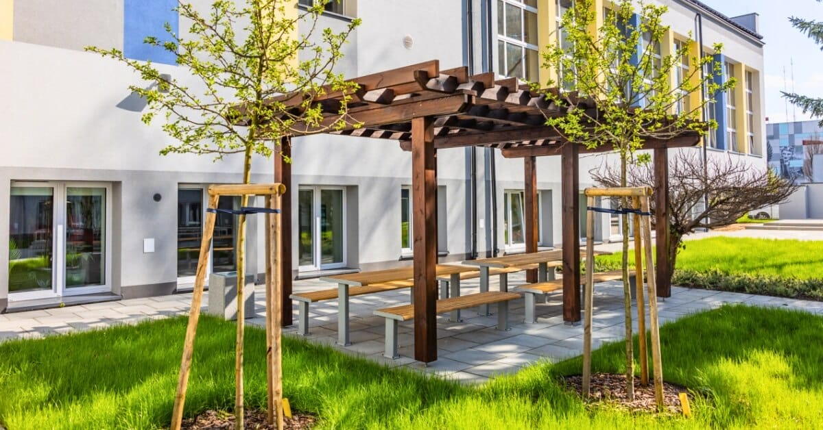 Houten picknicktafel met vaste bankjes en onderstel van staal in betegelde groene binnentuin