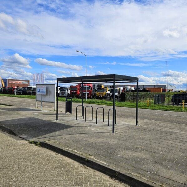 fietsoverkapping direct online kopen voor carpool Fietsoverkapping met vijf fietsnietjes en prullenbak op een industrieterrein langs de weg met geparkeerde vrachtwagens.