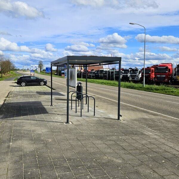 fietsoverkapping kopen voor carpoolplaats Rijwieloverkapping met fietsnietjes aan een parkeerplaats langs een industriële weg met vrachtwagens.
