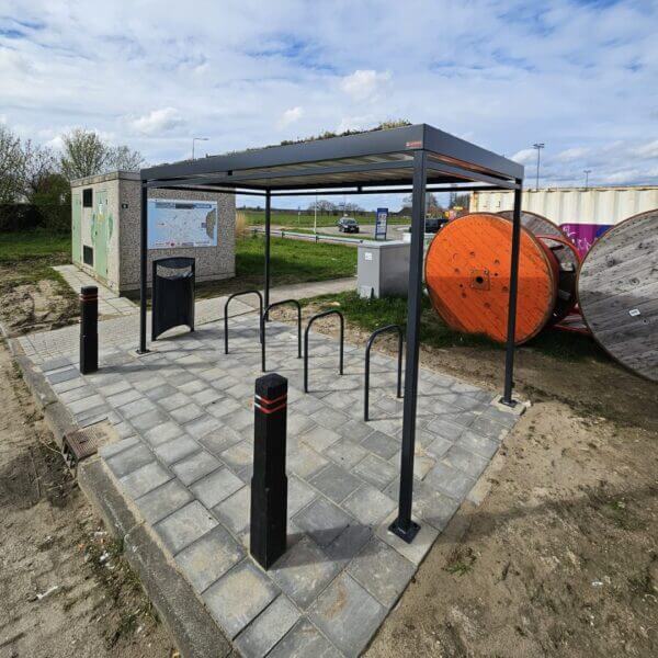 fietsoverkapping-umfeldt-aanschaffen-reitdiep Fietsoverkapping met zwarte fietsnietjes en sedumdak op een betegeld plein, omringd door paaltjes en straatmeubilair.