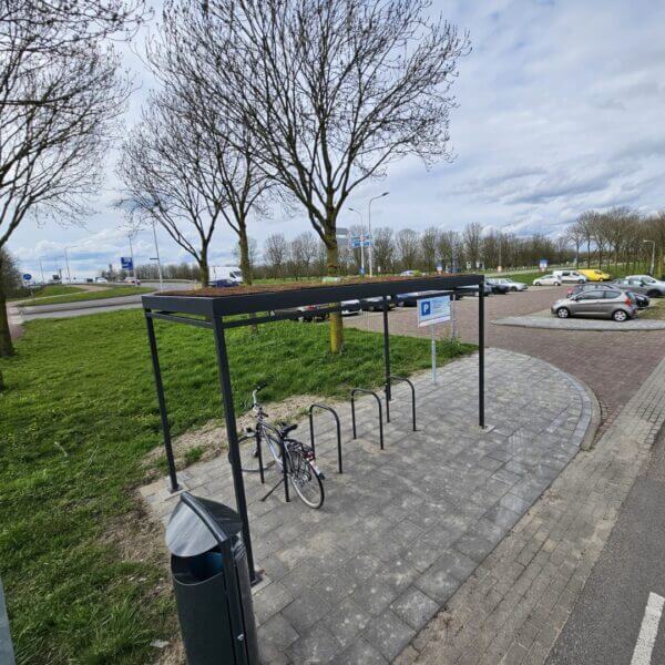 rijwieloverkapping-4x2m-sedum-dak-kopen Rijwieloverkapping 4x2m in antraciet met fietsnietjes en sedumdak geplaatst op tegels van een carpoolplaats