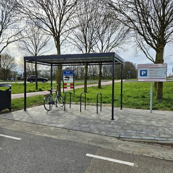rijwieloverkapping-kopen-umfeldt-reitdiep Rijwieloverkapping met zwarte fietsnietjes op een carpoolplaats in Eist langs de A325, met één geparkeerde fiets onder het afdak en informatieborden op de achtergrond..