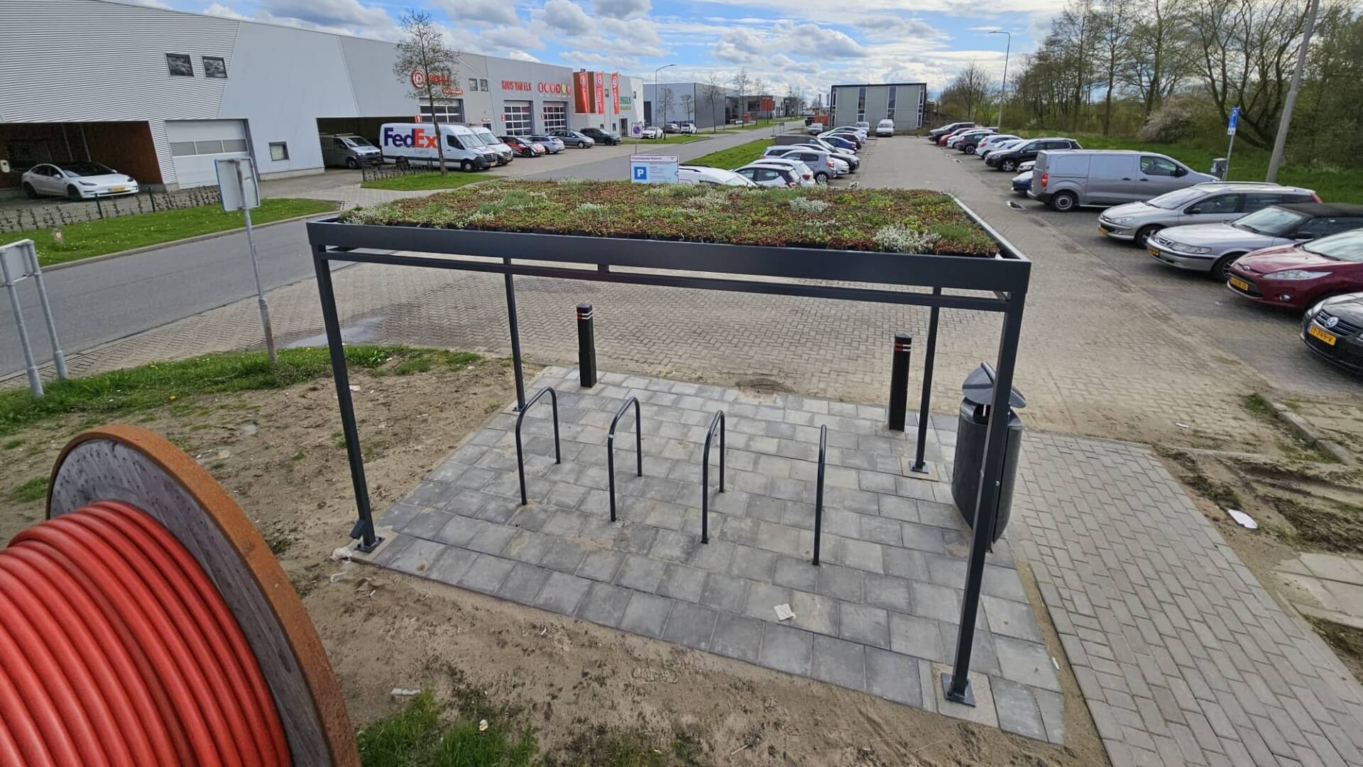 Zwarte rijwieloverkapping met sedumdak en vijf fietsnietjes op bedrijventerrein.