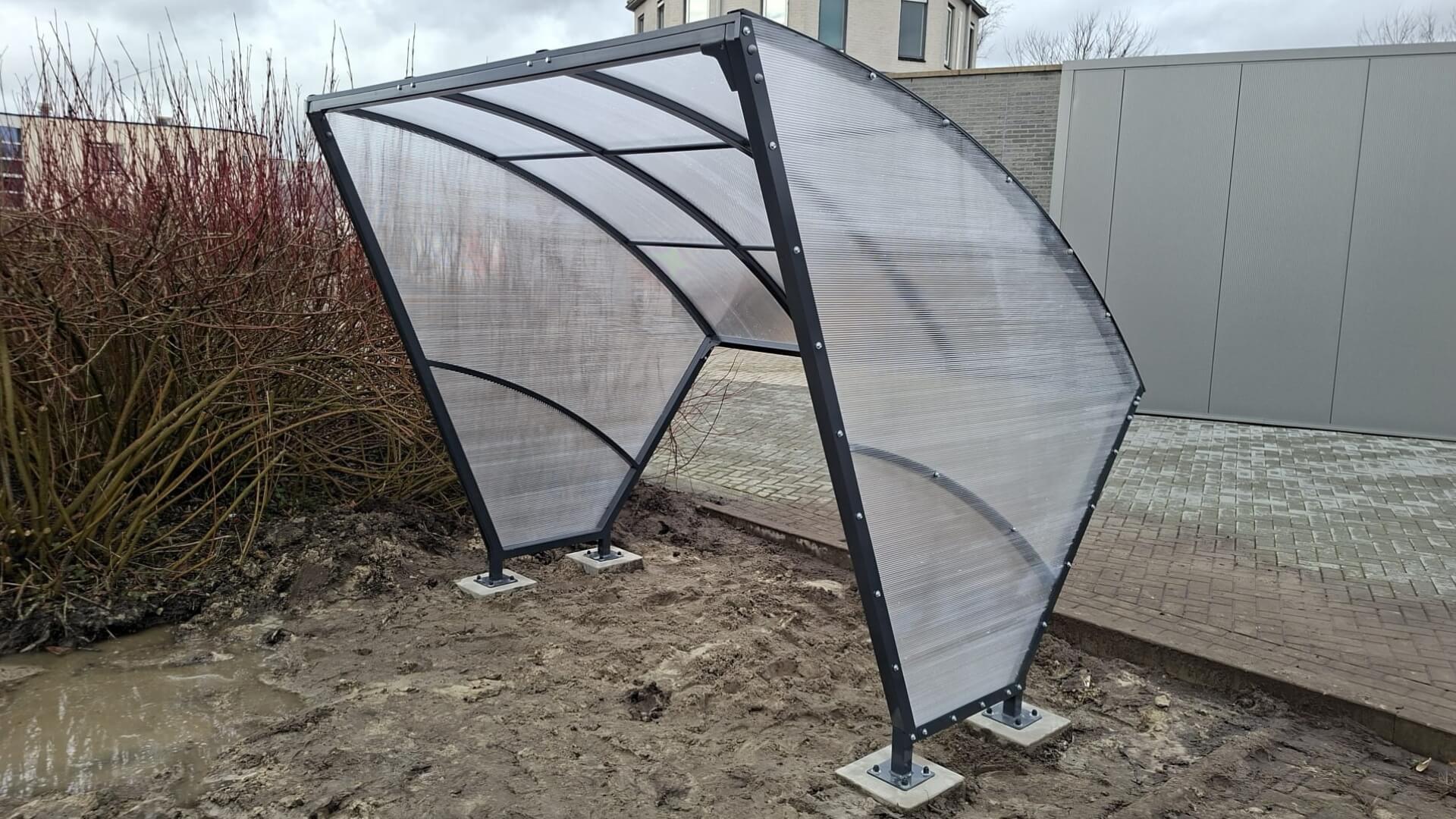 Kleine fietsoverkapping geplaatst op betonpoeren op een ondergrond van zand