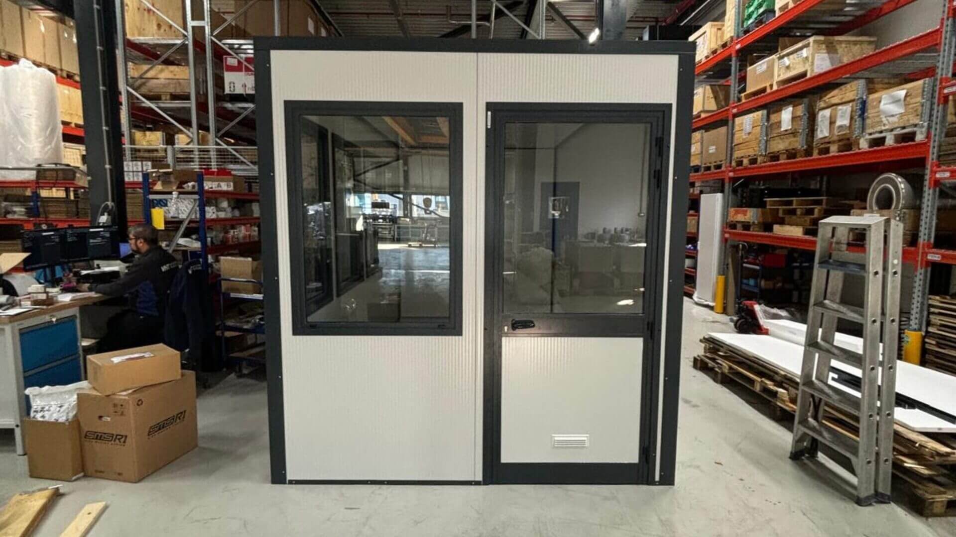 Kleine kantoorunit van 4x2 meter in een magazijnomgeving.