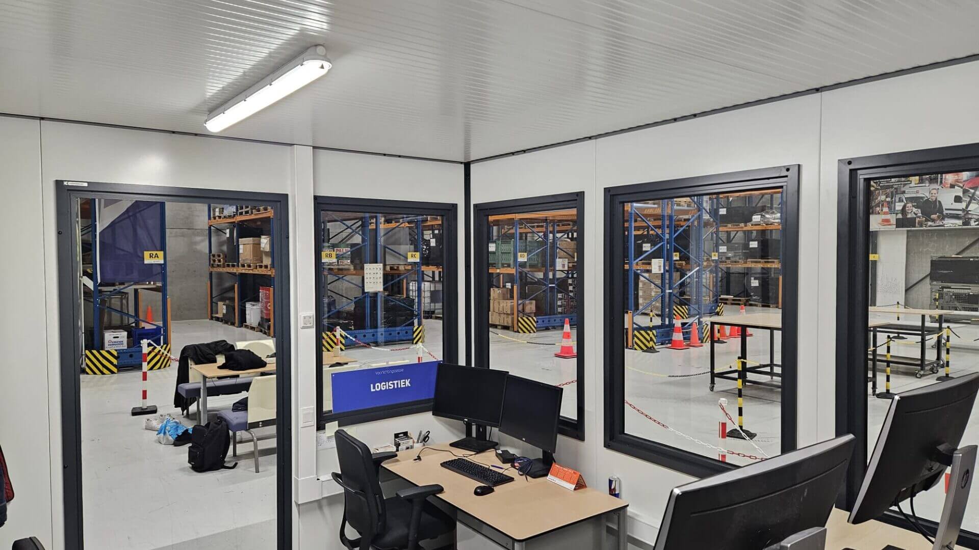 Binnenkant van een kantoorunit met werkplek, uitzicht op logistiek magazijn.