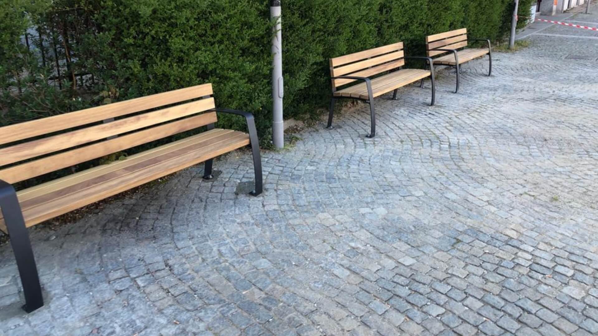 Seniorenparkbanken met verhoogd zitvlak en armleuningen langs wandelpad, houten buitenbanken met stalen frame voor ouderen.