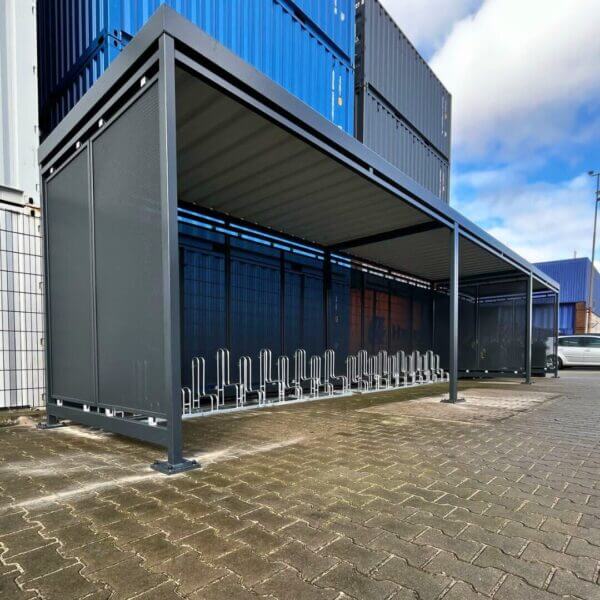 Moderne fietsoverkapping met rookabri bestellen Fietsoverkapping met geïntegreerde fietsenrekken tegen een achtergrond van gestapelde zeecontainers op een industrieterrein.