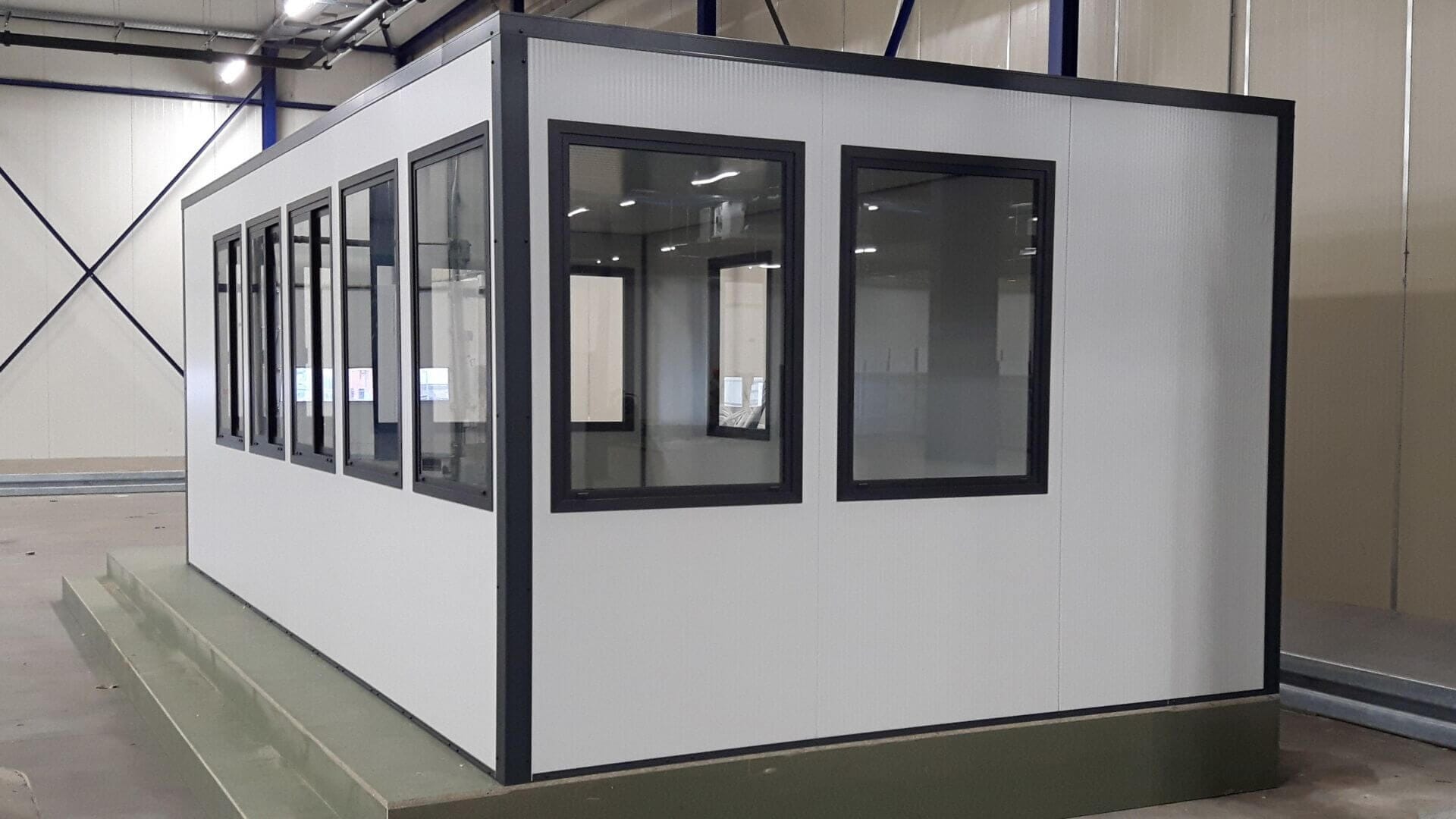 Prefab kantoorunit voor binnen met meerdere ramen, geplaatst in een industriële hal.