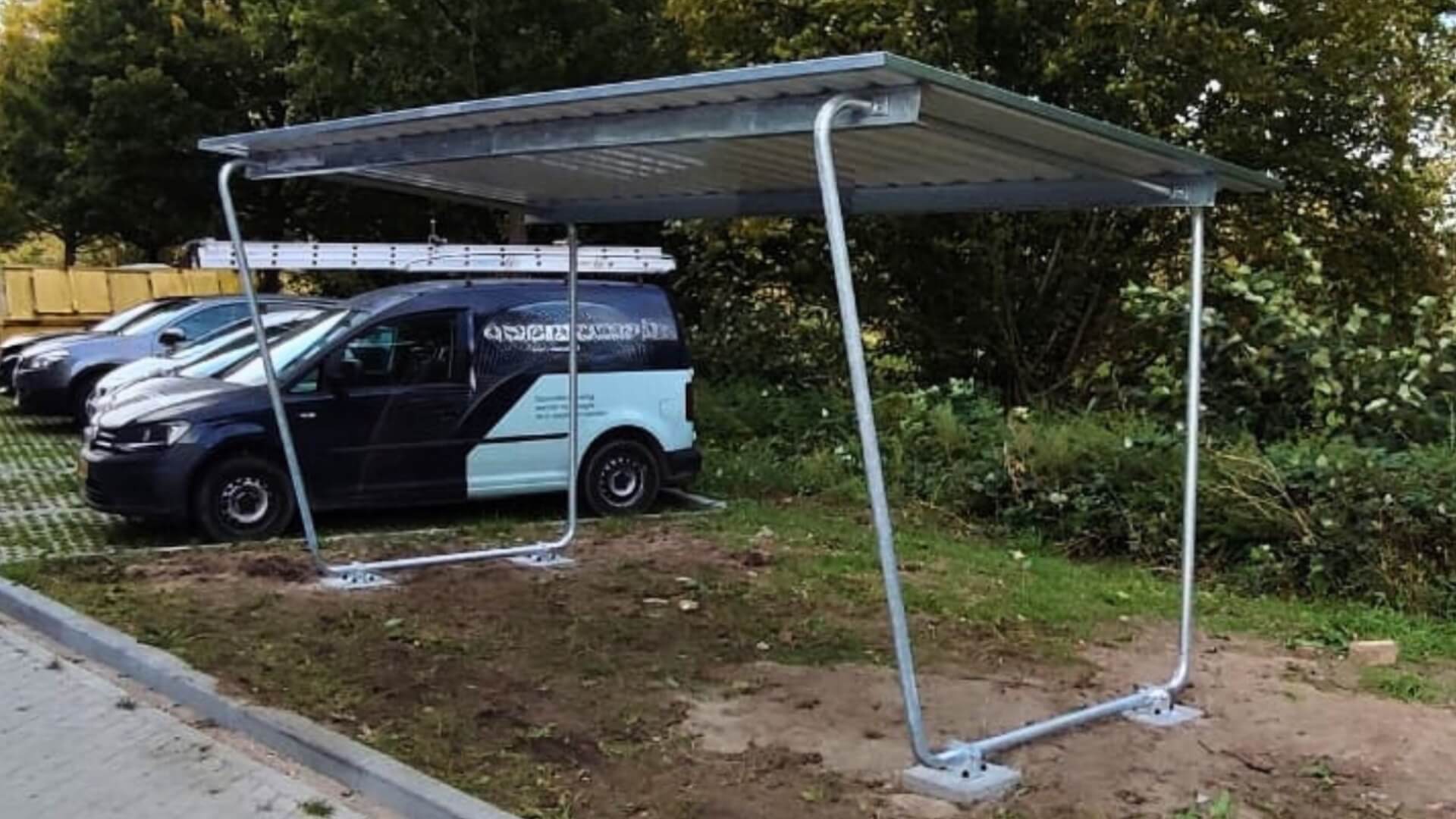 Bouwpakket fietsenhok ken met metalen dak op grasveld naast parkeerplaats