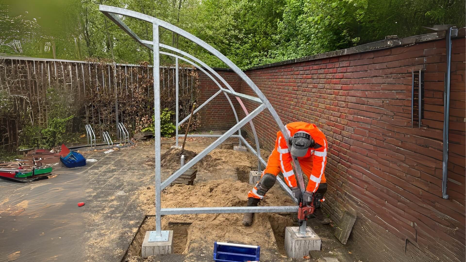 Monteur bevestigt stalen frame van een grote bouwpakket fietsoverkapping op betonpoer tijdens installatie