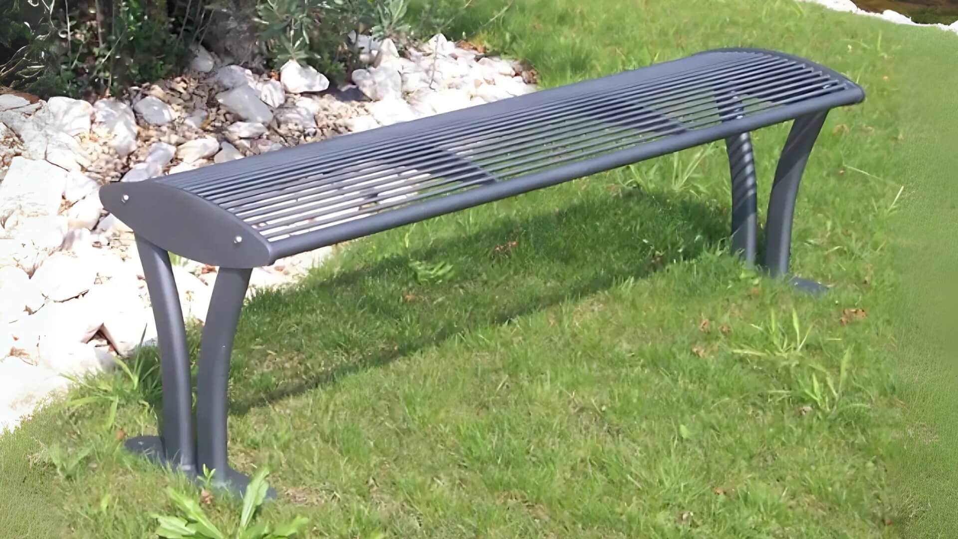 Zwarte metalen tuinbank zonder rugleuning, geplaatst op een grasveld naast een rotspartij met witte stenen.