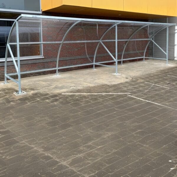 Prefab fietsenhok kopen Prefab fietsenhok met transparant dak en gegalvaniseerd staal frame, geplaatst bij een school.