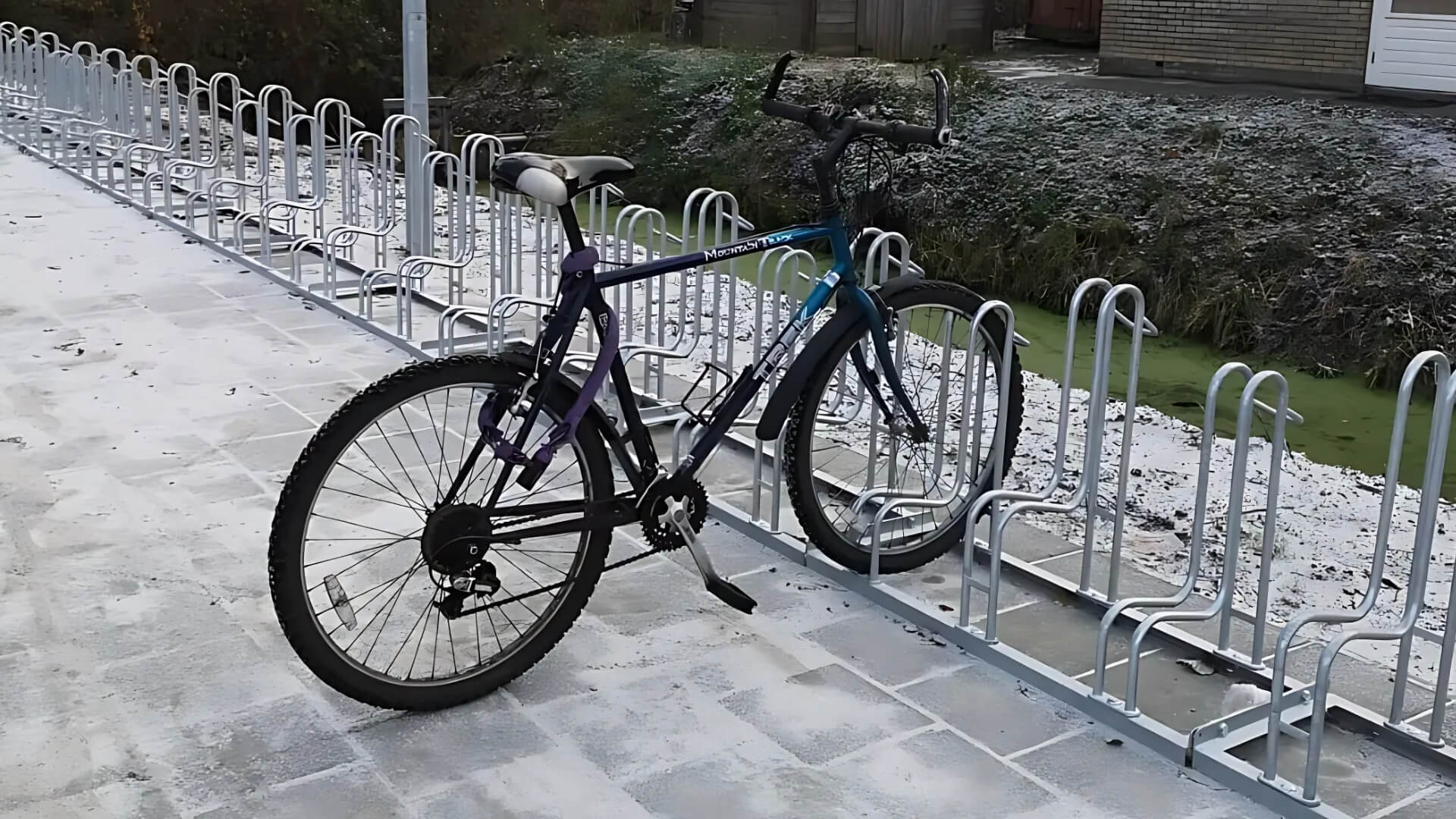 Verzinkt fietsenrek met fiets geplaatst op stoeptegels bij sportaccommodatie