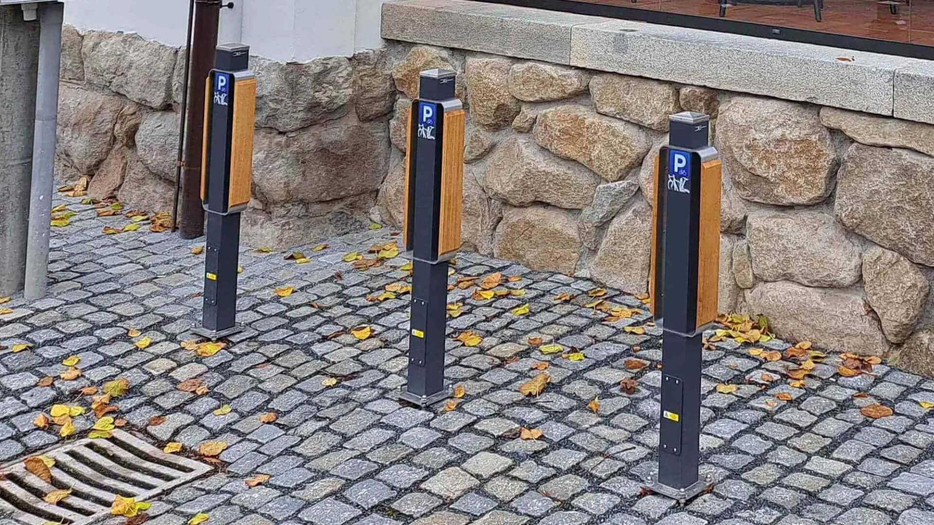 Moderne fietsoplaad punten met houtaccenten, geplaatst op een geplaveide stoep naast een stenen gevel