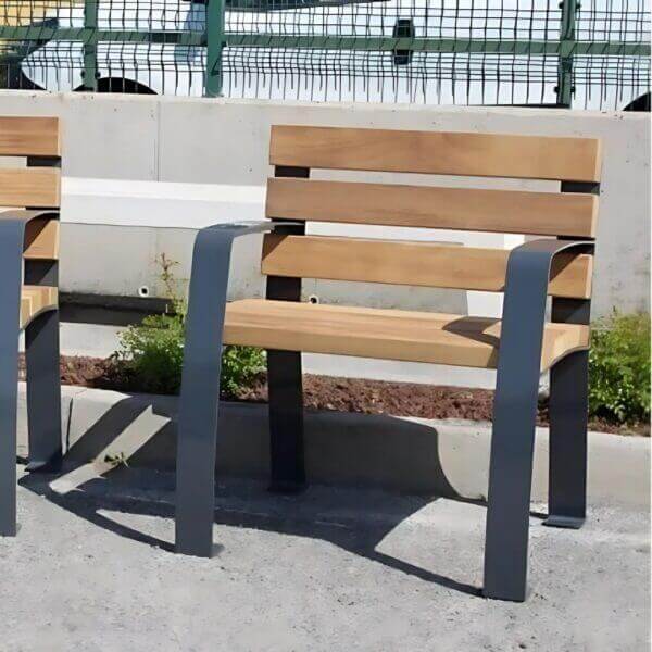 buitenstoel-senior-hoge-zitting-aanschaffen arkstoel Senior in buitenopstelling met houten zitvlak en rugleuning, zwart metalen frame.