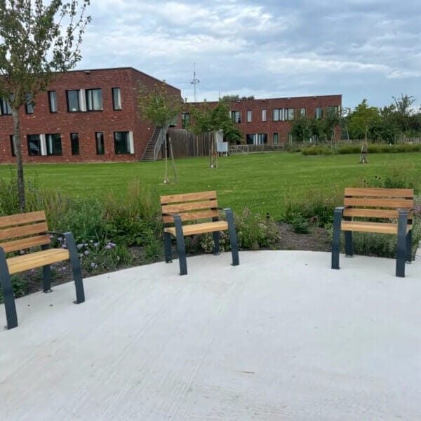 Parkstoel voor ouderen Parkstoelen met hoge zitting, speciaal ontworpen voor ouderen, geplaatst op een plein met groen en gebouwen op de achtergrond.
