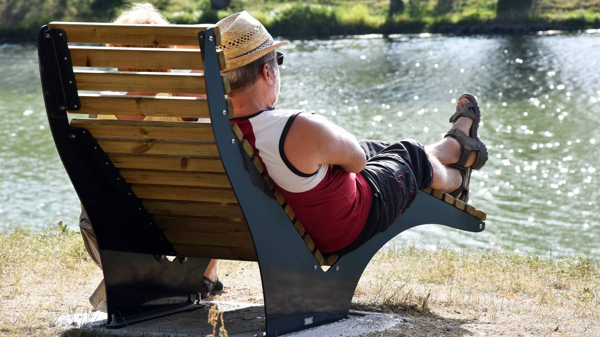 Houten loungestoel voor buiten met man aan het water in de zon.