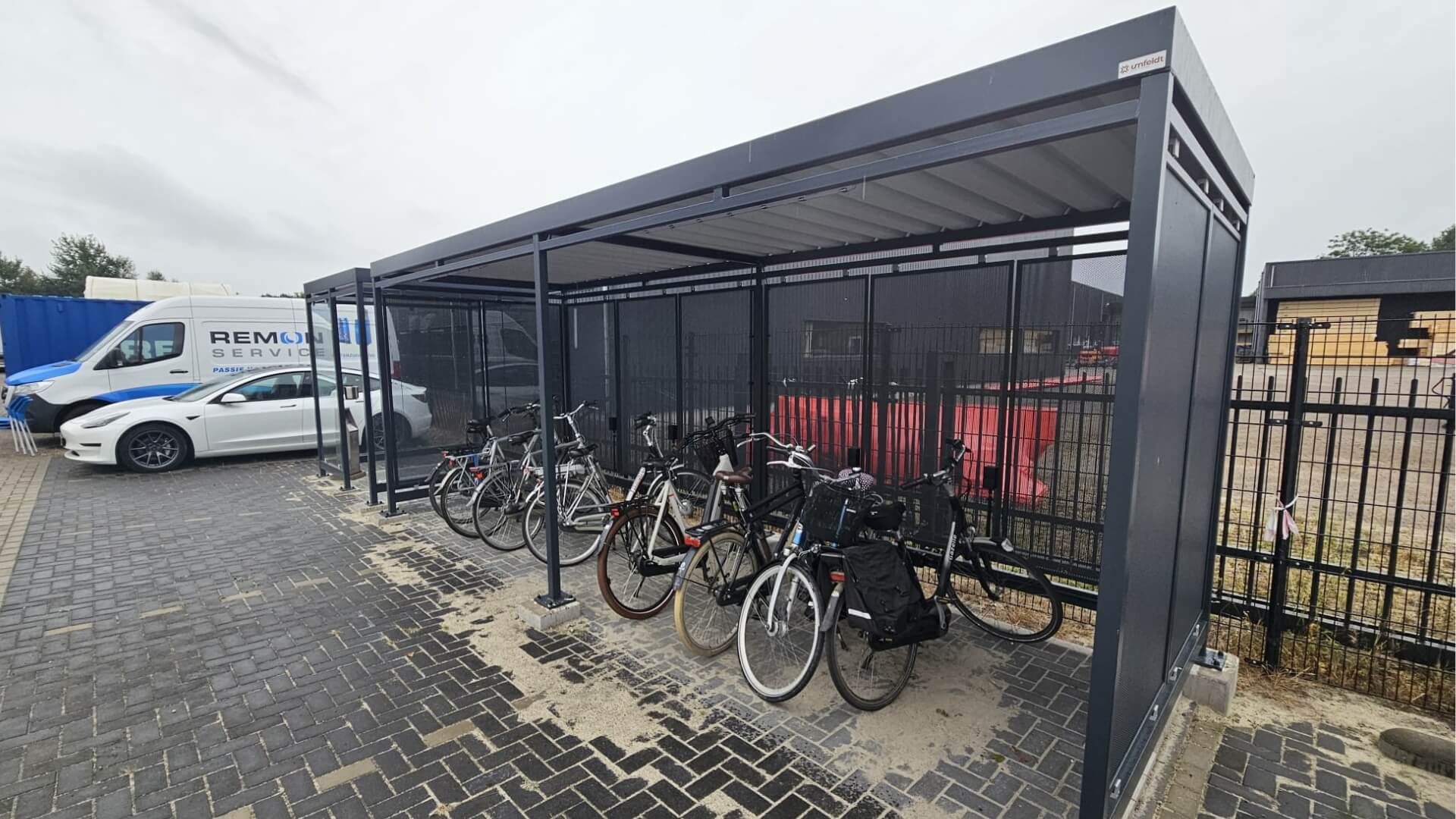Zwarte fietsoverkapping met fietsen en rookruimte van glas, geplaatst op parkeerplaats bij bedrijfspand
