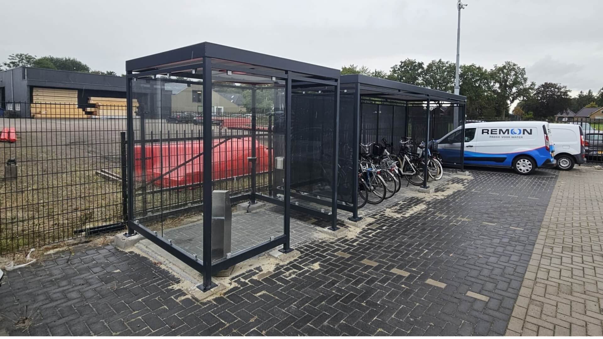 Rookabri voor buiten met glazen wanden en stalen frame naast fietsoverkapping op bedrijfsterrein