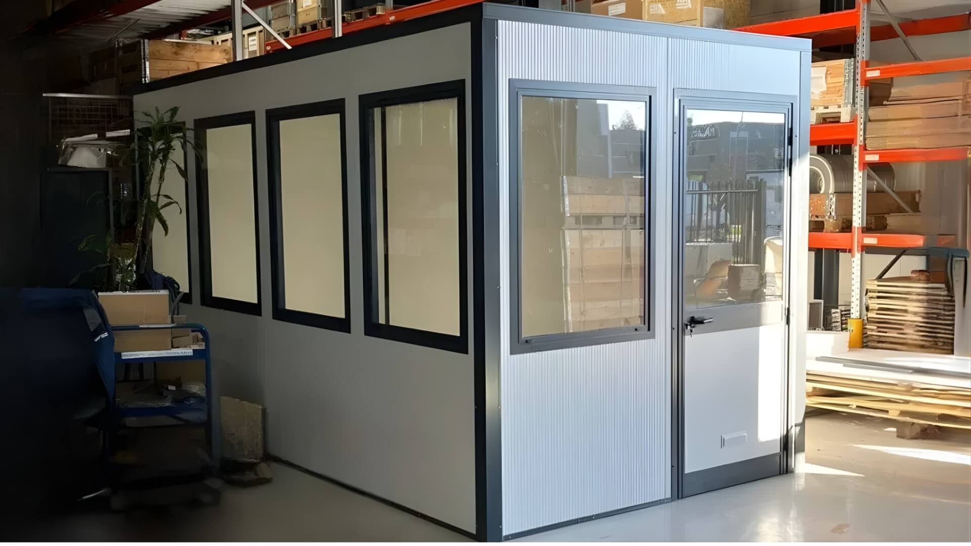 Prefab bureelunit van circa 2x4 meter geplaatst in magazijn van een bedrijfspand en voorzien van ramen en deuren.