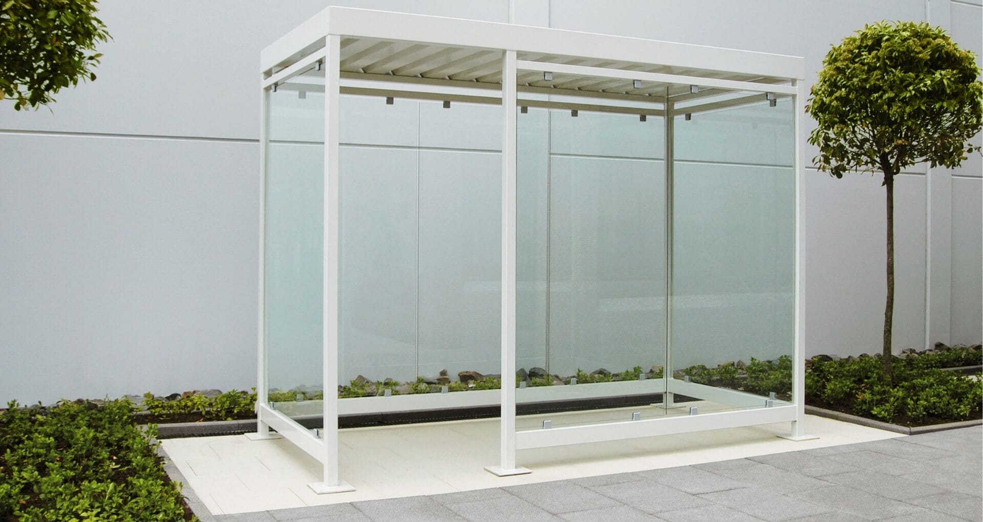 Witte rookoverkapping van staal en glas geplaatst naast een modern gebouw met groenvoorziening